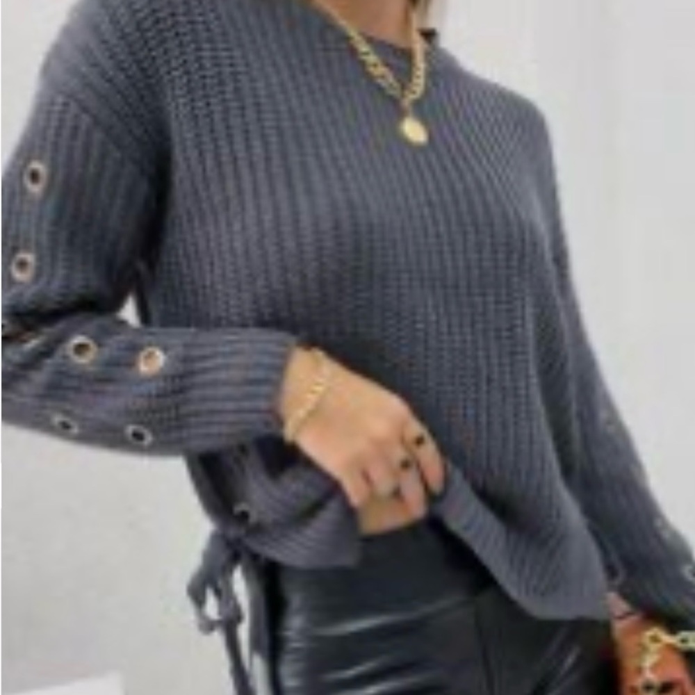 A dark gray knit sweater with side ties and grommet detailing on the sleeves.